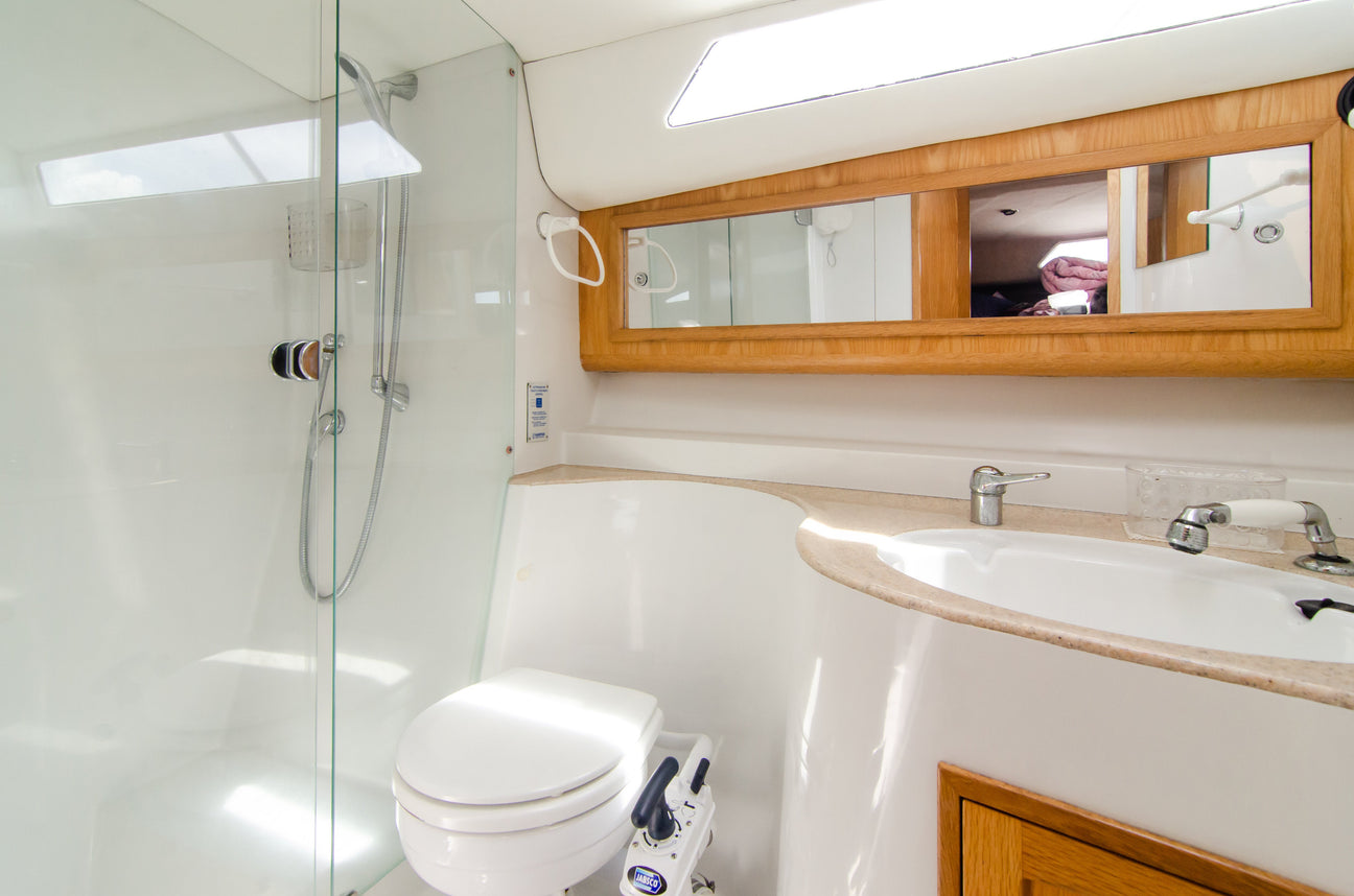 Modernes Badezimmer auf einem Boot mit weißem WC, Spiegeln, Waschbecken und einer Glasdusche mit verchromter Handbrause.