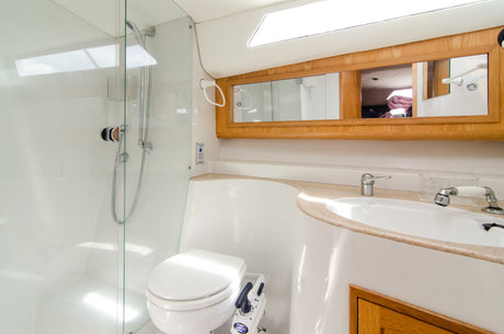 Modernes Badezimmer auf einem Boot mit weißem WC, Spiegeln, Waschbecken und einer Glasdusche mit verchromter Handbrause.