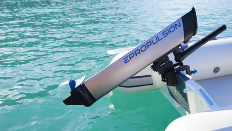 Nahaufnahme eines silber-blauen Elektromotors der Marke „ePropulsion“, der am Heck eines weißen Schlauchboots montiert ist. Das Boot schwimmt auf klarem türkisfarbenem Wasser.
