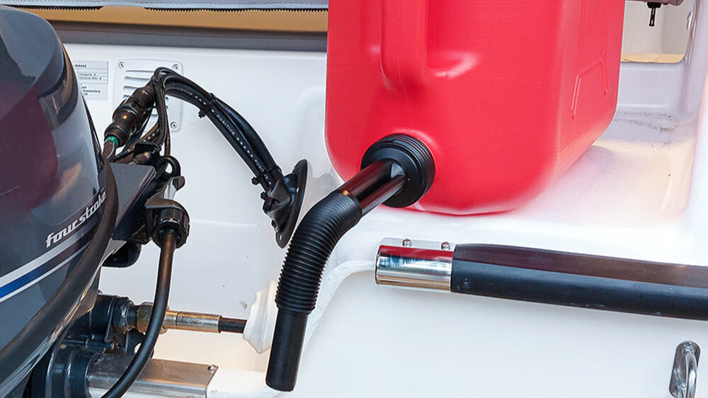 Nahaufnahme eines Außenbordmotors mit angeschlossenem schwarzem Treibstoffschlauch, der zu einem roten Benzinkanister führt, der sicher im Boot verstaut ist.