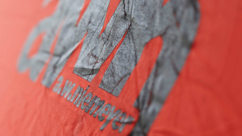 Nahaufnahme des aufgedruckten Logos „awn a.w. niemeyer“ auf einem roten, leicht zerknitterten Stoff – vermutlich eine Rettungsweste.