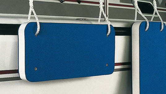 Rechteckige, flache Bootsfender in Blau mit weißer Kante, die mithilfe von weißen Seilen an der Bordwand eines Segelboots befestigt sind. Die Fender schützen das Boot beim Anlegen vor Beschädigungen.