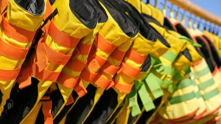 Mehrere farbenfrohe Rettungswesten in Gelb, Orange und Grün hängen ordentlich nebeneinander an einer Reling – bereit für den Einsatz an Bord.