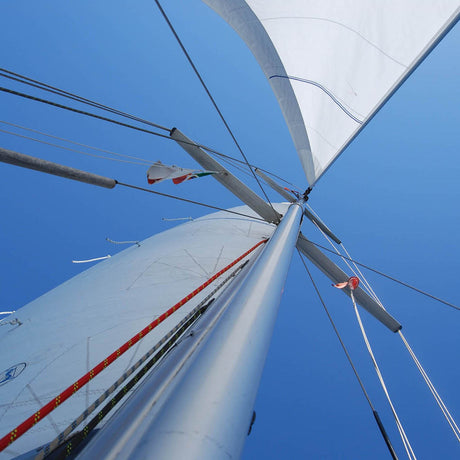 Blick nach oben am Aluminiumsegelmast mit gesetzten weißen Segeln vor klarem, blauem Himmel.