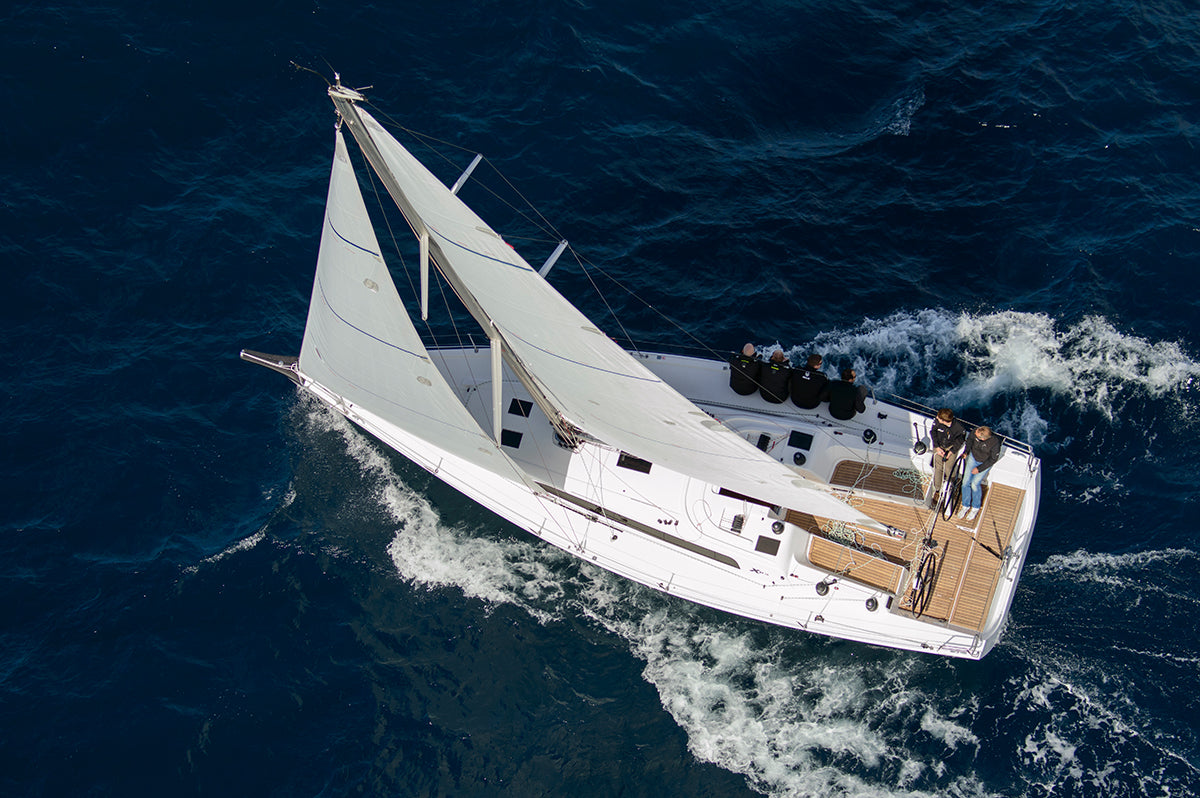 Segelyacht mit gesetzten weißen Segeln fährt bei Wind durch tiefblaues Meer, mehrere Personen an Bord.