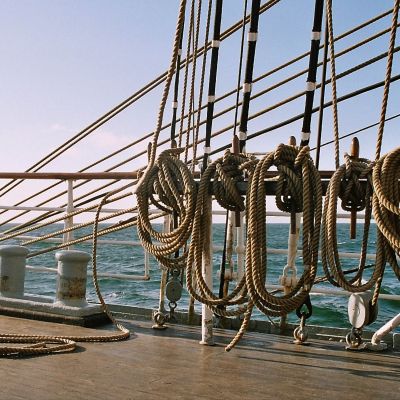 Mehrere Seile sind ordentlich aufgerollt und an einem traditionellen hölzernen Segelschiff befestigt, das auf offener See fährt.